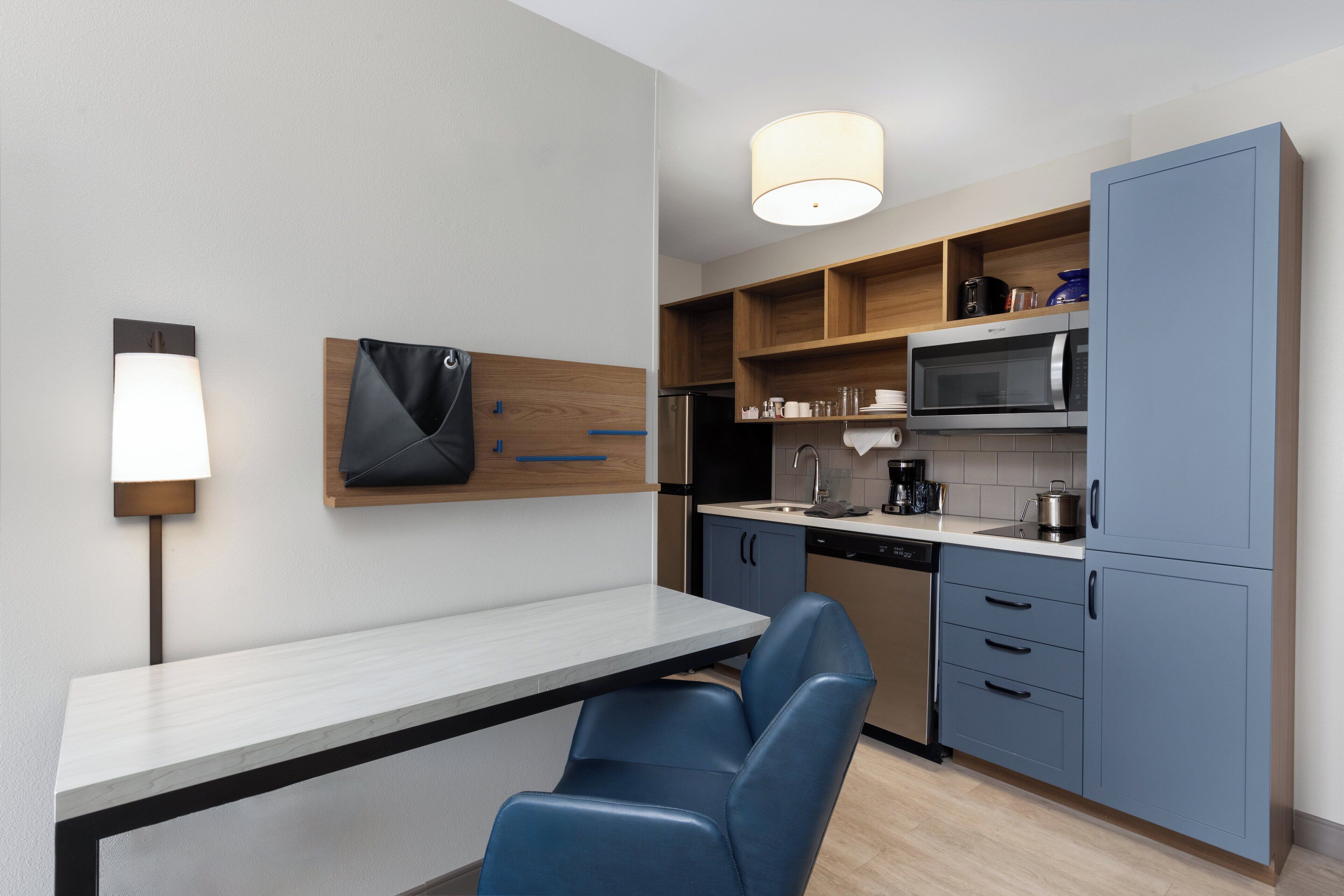 A modern kitchen with a white countertop, blue chairs, and wooden cabinets.