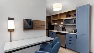 A modern kitchen with a white countertop, blue chairs, and wooden cabinets.