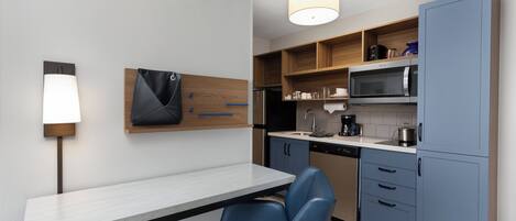 A modern kitchen with a white countertop, blue chairs, and wooden cabinets.