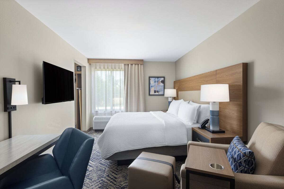 A hotel room with a bed, bedside tables, a desk, a chair, and a television.