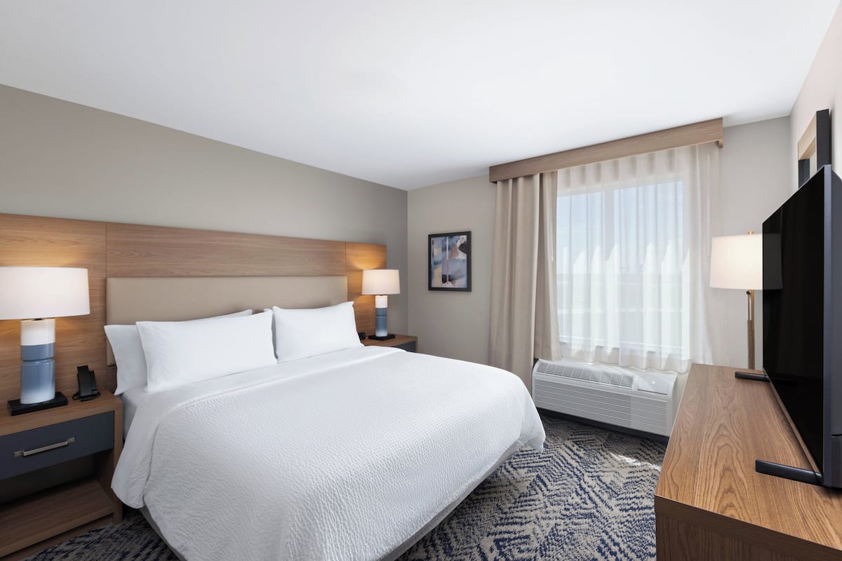 A hotel room with a large bed, two bedside tables with lamps, a TV, and a window with curtains.