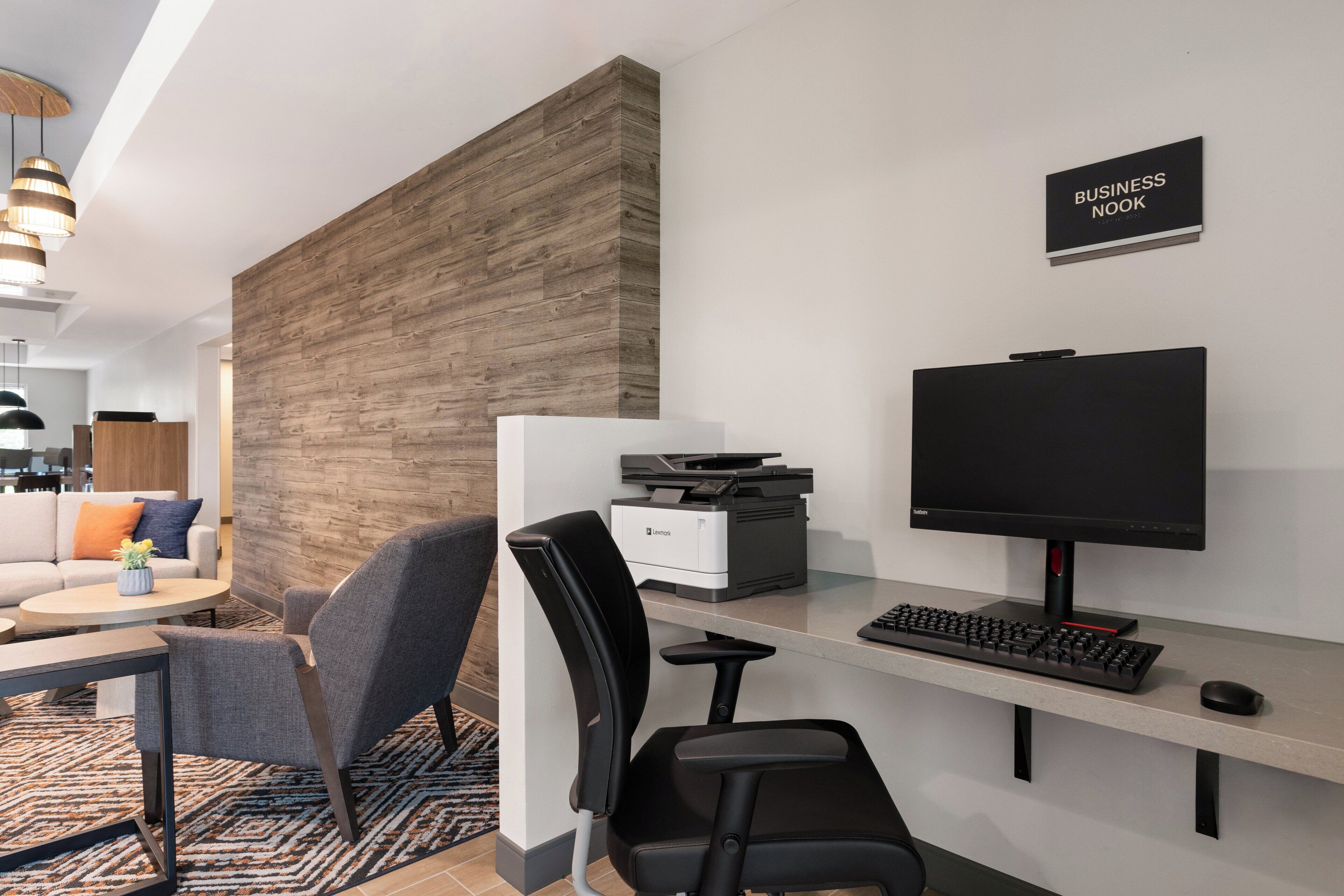 A modern office space with a desk, computer, printer, and a TV. There is a sign that reads "BUSINESS NOOK" on the wall.
