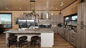 A modern kitchen with a large island, bar stools, stainless steel appliances, and wooden cabinetry. - Splashin' Mountain Retreat - Sip Cocktails Fireside, Swim with Fountains & Project Movies! (Sevierville)