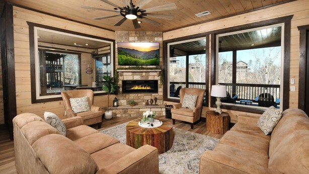 A cozy living room with a fireplace, comfortable seating, and large windows offering views of the surrounding area. - Splashin' Mountain Retreat - Sip Cocktails Fireside, Swim with Fountains & Project Movies! (Sevierville)