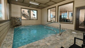 An indoor swimming pool with stone flooring and a metal ladder. - Splashin' Mountain Retreat - Sip Cocktails Fireside, Swim with Fountains & Project Movies! (Sevierville)