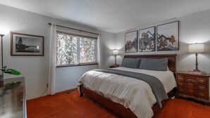 A bedroom with a large bed, a nightstand, a lamp, and a window with curtains. - NEW - Truckee Cabin - Centrally Located (Truckee)