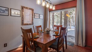 A dining area with a wooden table, chairs, and a chandelier. There are framed pictures on the wall and a window with a view of trees. - NEW - Truckee Cabin - Centrally Located (Truckee)