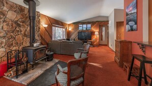A cozy living room with a stone wall, a fireplace, a sofa, and a television. - NEW - Truckee Cabin - Centrally Located (Truckee)