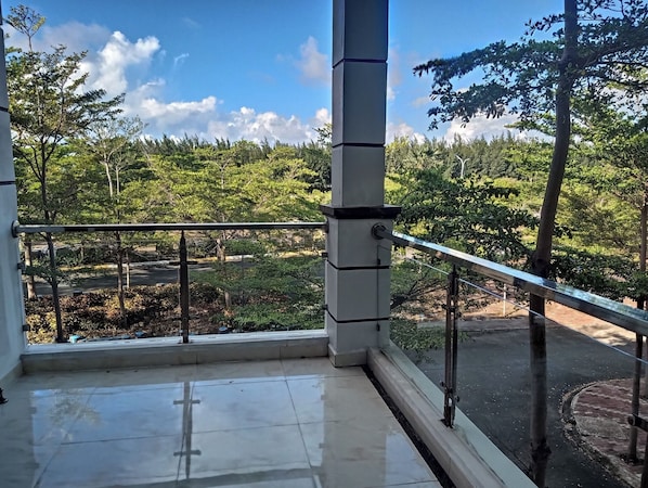 A balcony with a metal railing overlooking a garden with trees and a road.