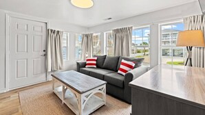 A modern living room with a grey sofa, a wooden coffee table, and a view of a building through large windows.
