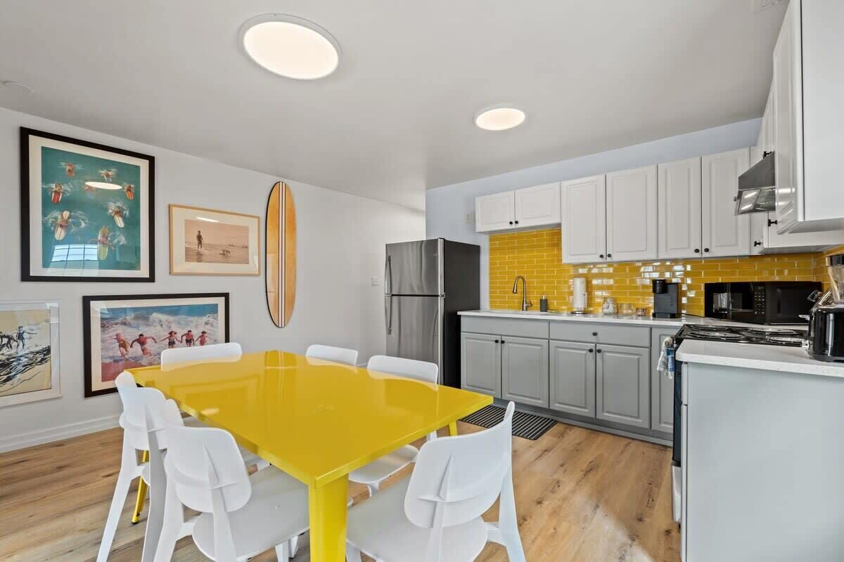 A modern kitchen with white cabinets, a yellow tiled backsplash, and a bright yellow dining table.