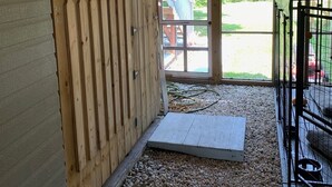 Un intérieur en bois, avec une porte en bois, une fenêtre et un sol recouvert de gravier.