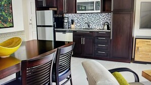 Una cocina moderna con armarios de madera oscura, un microondas y una cafetera. Hay una mesa de comedor con sillas y un tazón amarillo.