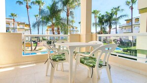 A balcony with a table and chairs, overlooking a swimming pool and palm trees. - Apartment in urbanization near the beach (Denia)