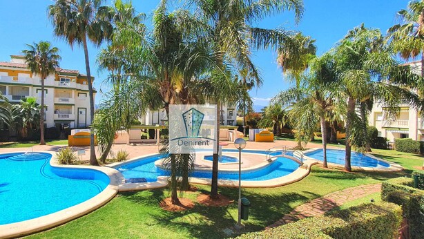 A resort with multiple swimming pools, palm trees, and a sign reading "Denirent". - Apartment in urbanization near the beach (Denia)