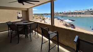 A balcony with a table and chairs, overlooking a beach with boats and a clear blue sky. - Beach Front Condo In Beautiful Lake Havasu Arizona (Lake Havasu City)