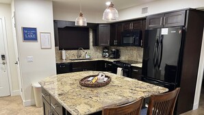 A kitchen with dark cabinets, a granite countertop, a black refrigerator, and a microwave. There are two wooden chairs with blue cushions. - Beach Front Condo In Beautiful Lake Havasu Arizona (Lake Havasu City)