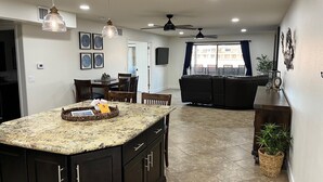 A kitchen with granite countertops, dark cabinetry, and pendant lighting. There is a dining area with a table and chairs, and a living area with a sofa and a ceiling fan. - Beach Front Condo In Beautiful Lake Havasu Arizona (Lake Havasu City)