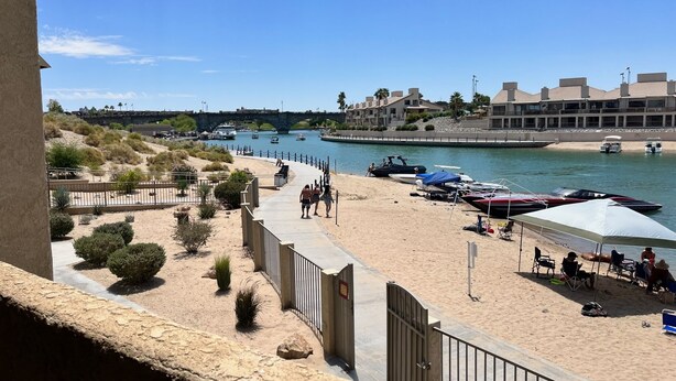 A beachside view with a sandy walkway, boats, and a building with multiple balconies. - Beach Front Condo In Beautiful Lake Havasu Arizona (Lake Havasu City)