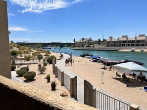 A beachside view with a sandy walkway, boats, and a building with multiple balconies.