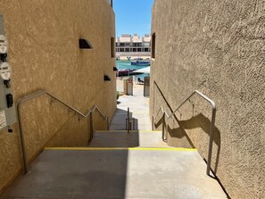 A concrete staircase leading to a pool area with a view of a building in the background.