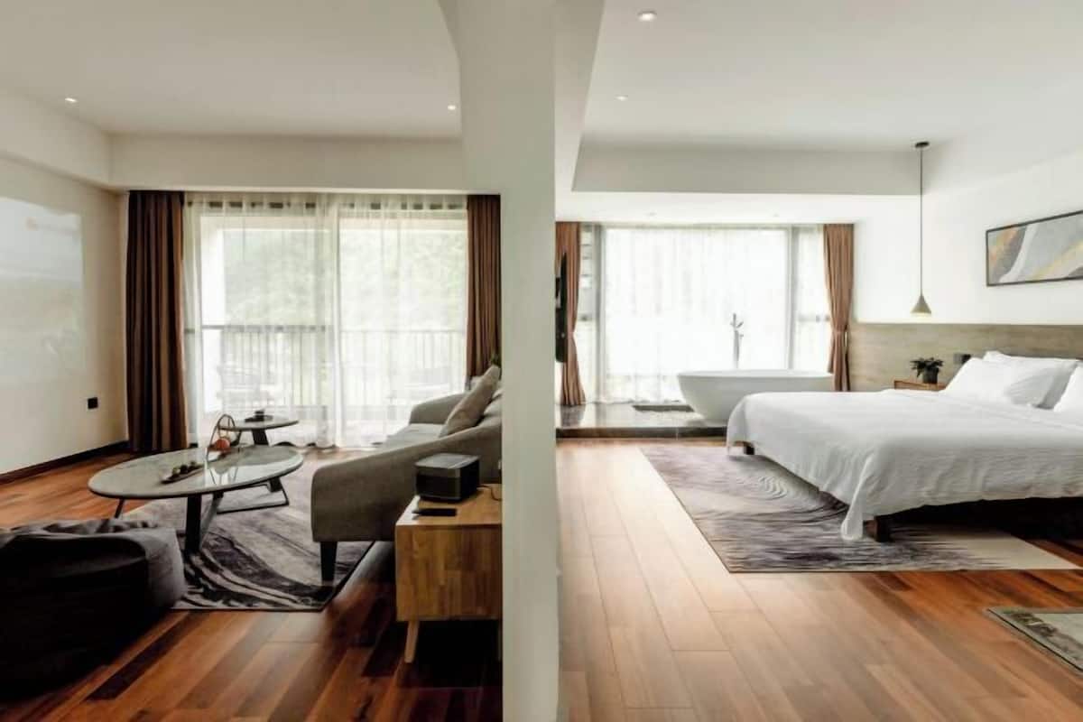 A modern hotel room with a large bed, a sofa, a coffee table, and a view of the outdoors.