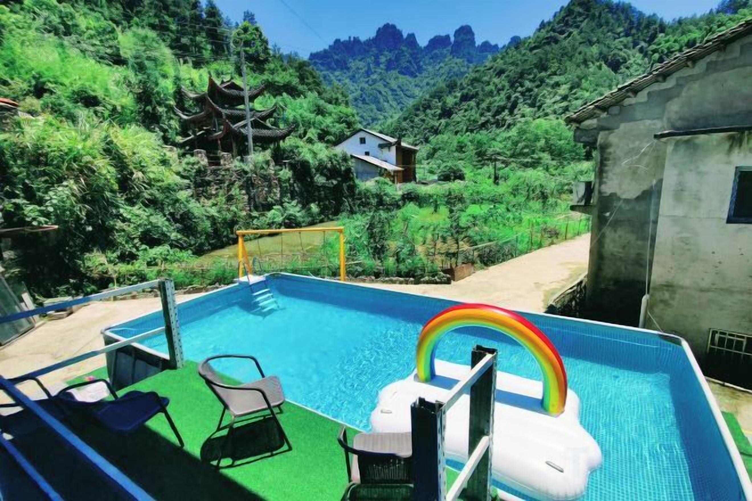 Una piscina con un flotador de arcoíris, rodeada de exuberante vegetación y montañas al fondo.