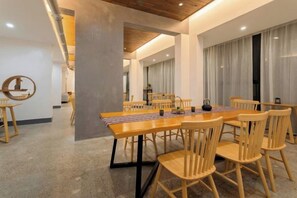 A dining area with a long wooden table and chairs, a modern ceiling with exposed beams, and a view of a cityscape through large windows. - Mini Inn (Zhangjiajie)