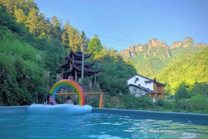A swimming pool with a rainbow inflatable arch, surrounded by lush greenery and traditional architecture. - Mini Inn (Zhangjiajie)