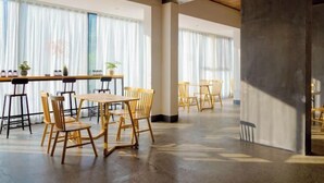 A spacious indoor area with wooden tables and chairs, large windows with sheer curtains, and a concrete pillar. - Mini Inn (Zhangjiajie)