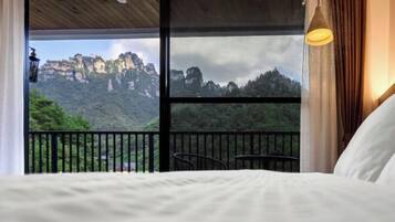 Quarto com uma janela grande, cama, poltrona e mesa.