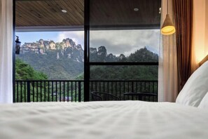 A bedroom with a large window, a bed, a chair, and a table.
