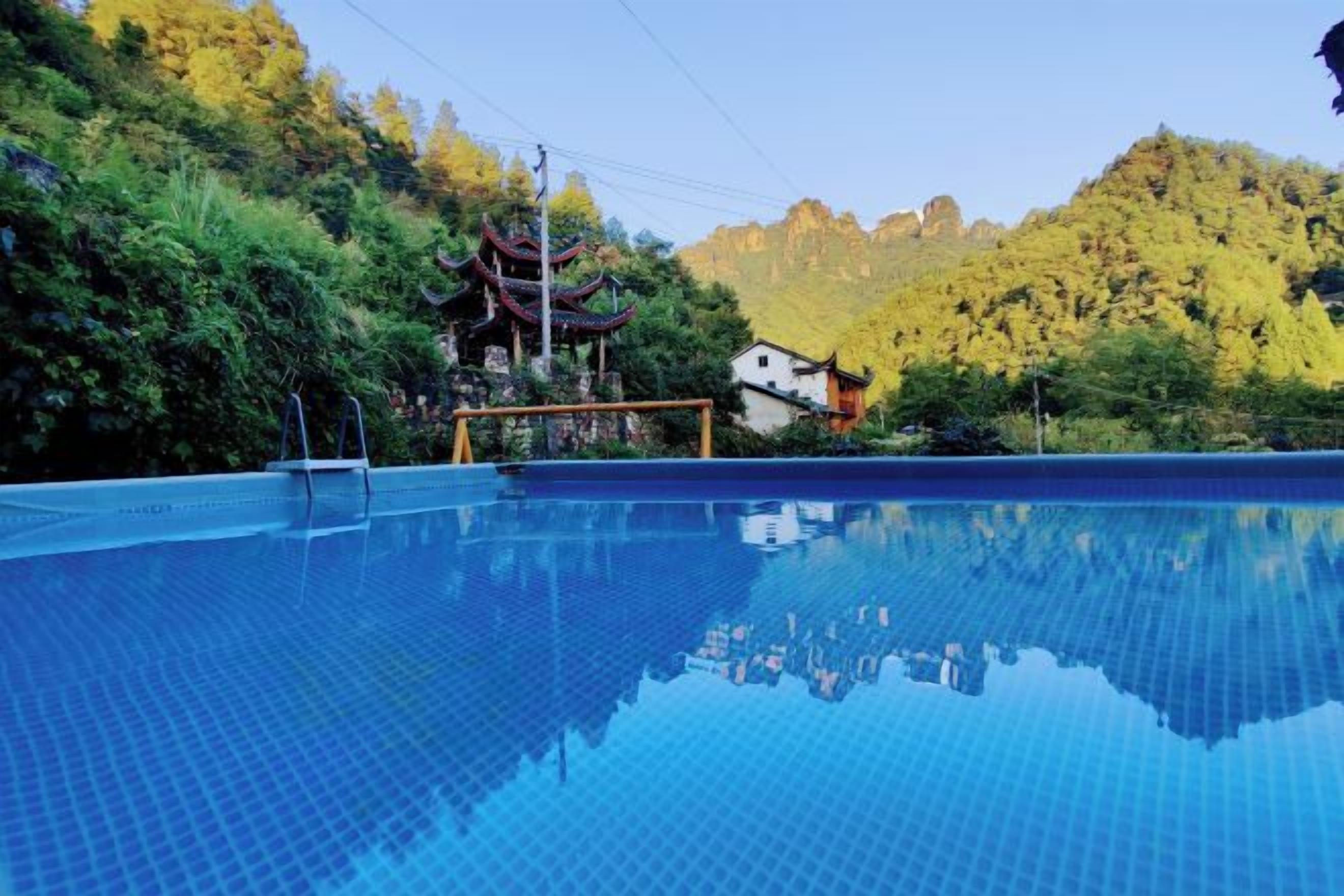 A swimming pool with a tiled surface, surrounded by greenery and a traditional building in the background.