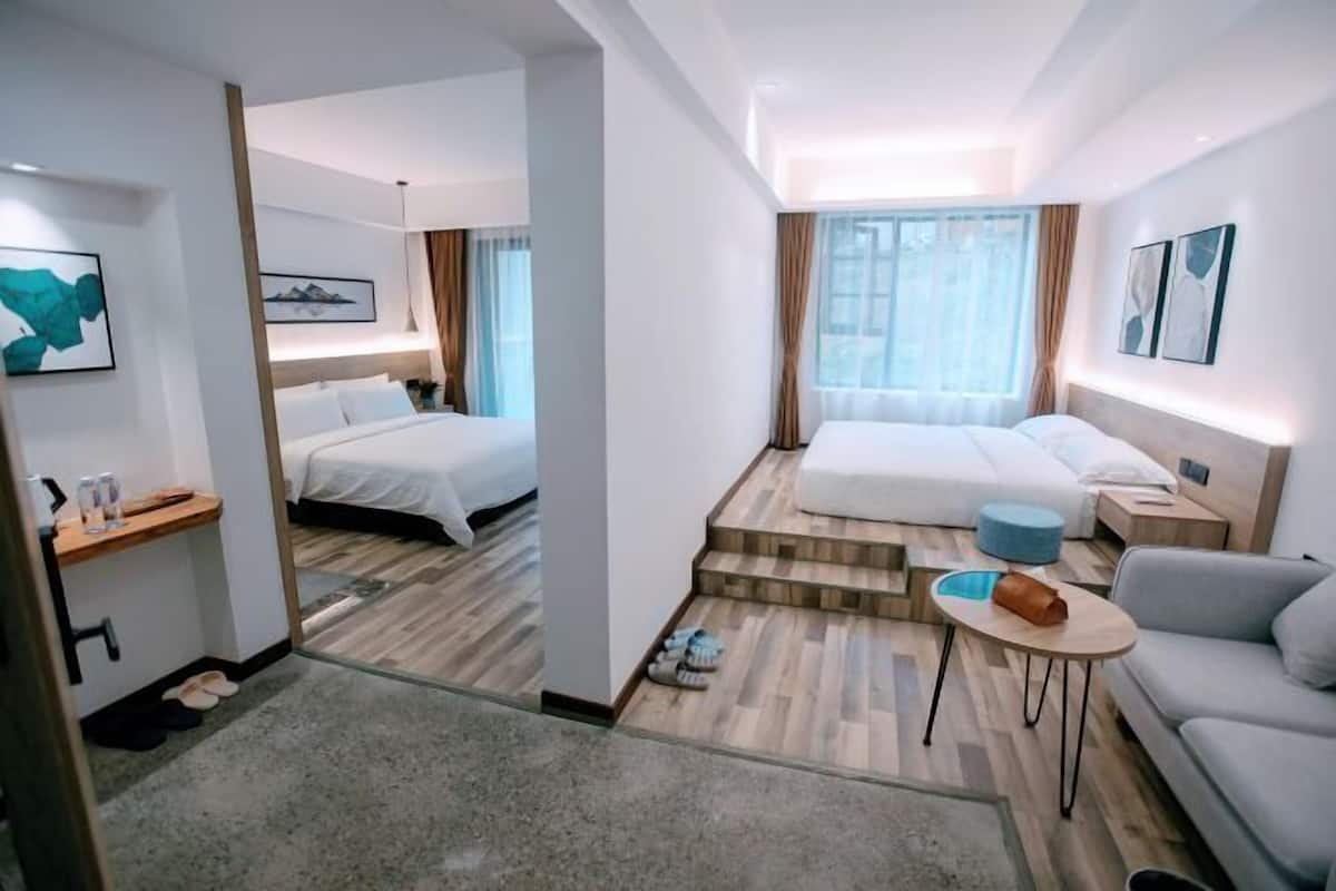 A hotel room with two beds, a sofa, a small table, and a shoe rack.