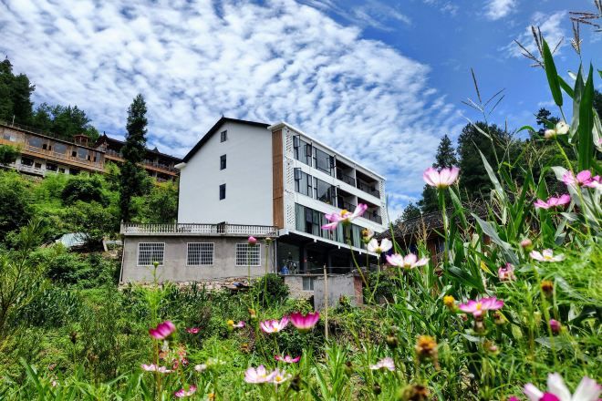 A multi-story building with a flat roof, surrounded by lush greenery and wildflowers.