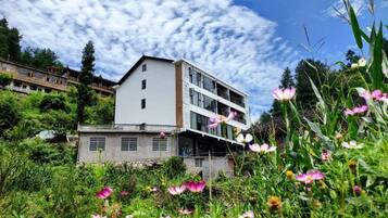 A multi-story building with a flat roof, surrounded by lush greenery and wildflowers.