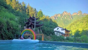 A swimming pool with a rainbow float, surrounded by lush greenery and traditional architecture. - Mini Inn (Zhangjiajie)