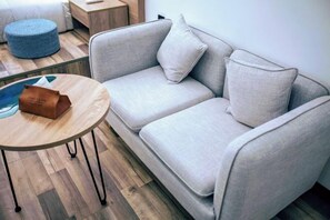 Una sala moderna con un sofá gris, una mesa redonda de madera y un otomano azul.