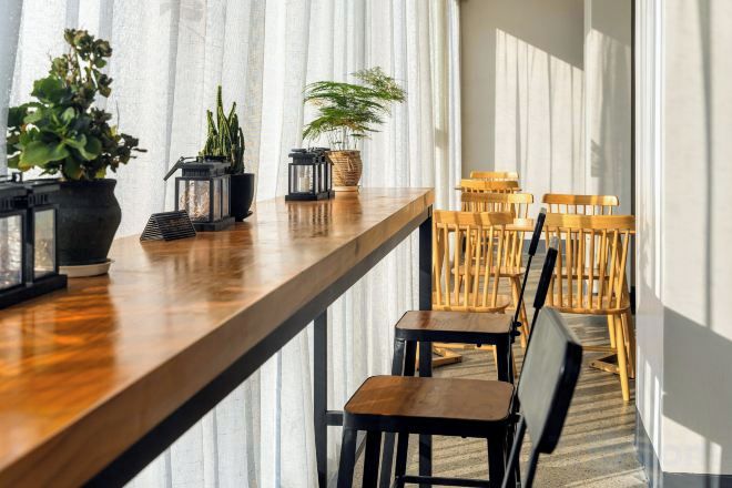A long wooden table with chairs, potted plants, and framed items.