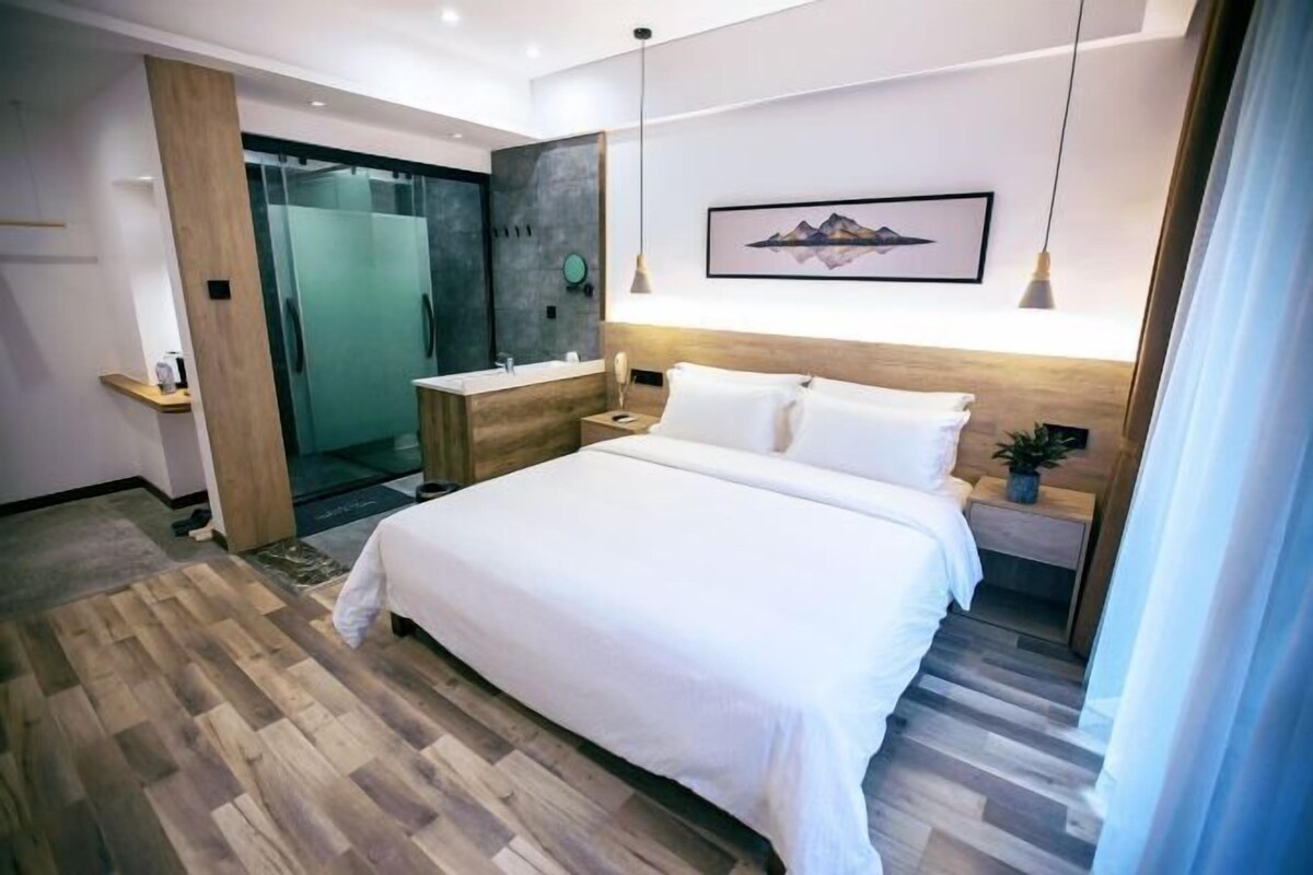 A modern bedroom with a large bed, a wooden floor, a glass shower, and a framed picture on the wall.