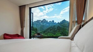 A hotel room with a large window, a bed, a red chair, and a small table. - Mini Inn (Zhangjiajie)