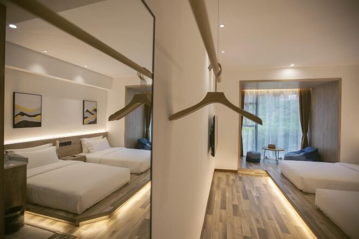 A hotel room with two beds, a seating area, and a hallway leading to another room.