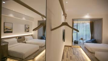 Quarto de hotel com duas camas, um espaço de estar e um corredor que leva a outro quarto.