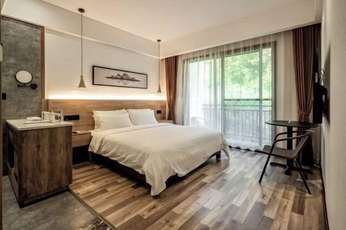 A hotel room with a bed, bedside table, chair, and a large window with curtains.