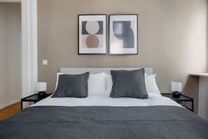 Quarto de hotel com uma cama, duas mesas de cabeceira, uma luminária em cada mesa e duas obras de arte abstratas emolduradas na parede.