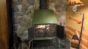 Un mur de pierres, un poêle à bois vert, un banc en bois et une lampe.