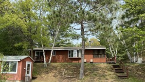 Une cabane de plain-pied avec un petit porche, une cheminée et un escalier menant à une terrasse.