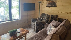 Un salon chaleureux avec un décor intérieur en bois, une grande fenêtre, un téléviseur fixé au mur et des meubles à motifs.