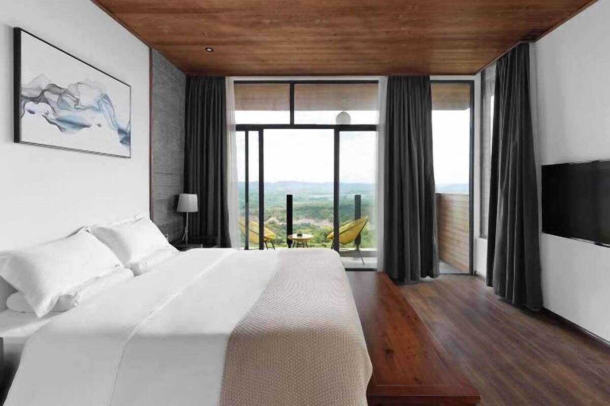 Habitación de hotel con una cama grande, televisión, un cuadro y balcón con vistas.