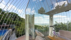 Una habitación con una gran cúpula de vidrio, una terraza de madera, un sofá, un telescopio y vistas a una piscina y zonas verdes.